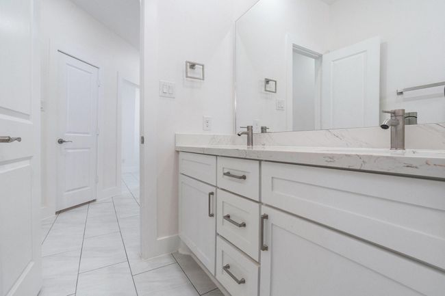 This bathroom features a sleek, modern design with a spacious marble countertop, dual sinks, and ample storage in white cabinetry. The neutral color scheme and large mirror enhance the room's brightness and openness. | Image 38