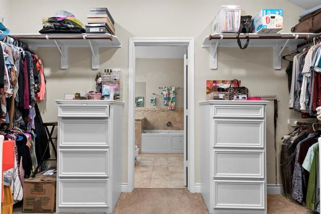 This is a spacious walk-in closet with built-in shelving and storage, leading directly into an en-suite bathroom, offering convenience and ample room for wardrobe organization. | Image 28