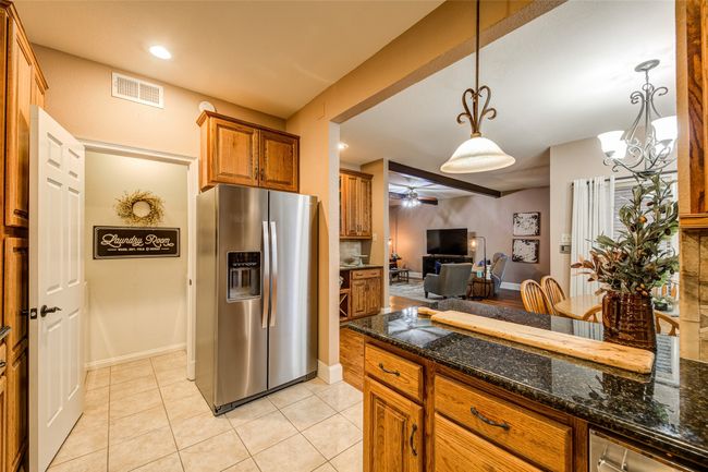 Kitchen featuring stainless steel refrigerator with ice dispenser, brown cabinetry, ceiling fan, open floor plan, and light tile patterned floors | Image 13