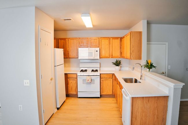 Kitchen with white appliances, light wood finished floors, light countertops, and a peninsula | Image 11
