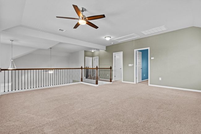 Carpeted empty room with attic access, a ceiling fan, vaulted ceiling, and baseboards | Image 23