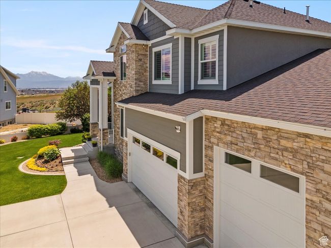 View of property exterior with stone siding, a shingled roof, an attached garage, a yard, and a mountain view | Image 4