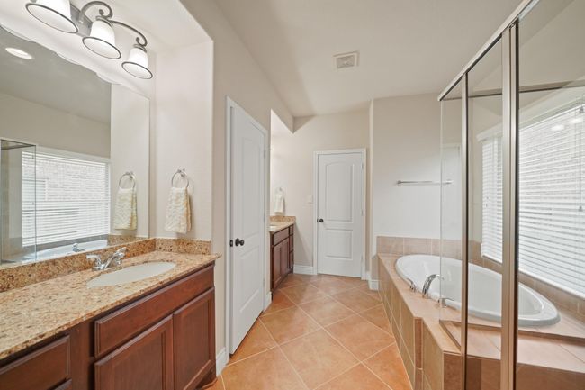 This spacious bathroom features a dual-sink vanity with granite countertops, a large mirror, and ample lighting. It includes a glass-enclosed shower, a separate soaking tub, and tiled flooring, offering a bright and elegant atmosphere. | Image 21