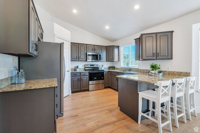 Kitchen featuring stainless steel appliances, a peninsula, lofted ceiling, a breakfast bar, and light wood finished floors | Image 5