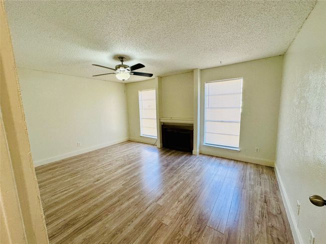 Unfurnished living room with wood finished floors, baseboards, a textured ceiling, ceiling fan, and a fireplace | Image 8