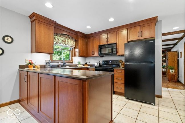 kitchen featuring black appliances, a peninsula, dark countertops, light tile patterned floors, and recessed lighting | Image 11