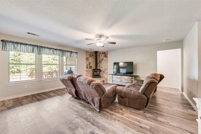 Living room with visible vents, a wood stove, a ceiling fan, a textured ceiling, and light wood finished floors | Image 8