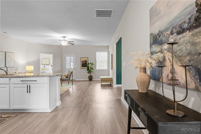 Kitchen with light wood-type flooring, white cabinets, light stone counters, a ceiling fan, and a sink | Image 10