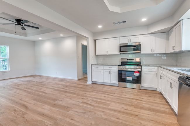 Kitchen featuring a raised ceiling, visible vents, light wood-type flooring, baseboards, and appliances with stainless steel finishes | Image 12
