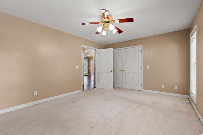 Unfurnished bedroom with light colored carpet, a chandelier, ceiling fan, and a closet | Image 7