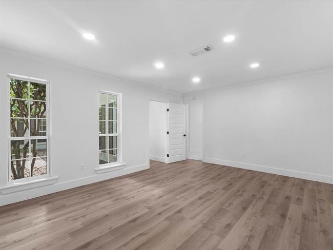 This room features bright, open space with light wood flooring and recessed lighting. Large windows allow for natural light, and a white door provides access to another area. Perfect for customization and versatile use. | Image 21