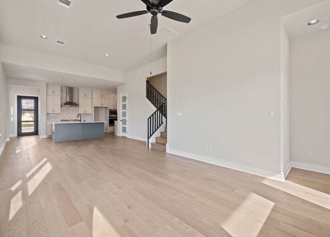 Unfurnished living room with baseboards, a ceiling fan, stairway, and light wood-type flooring | Image 9