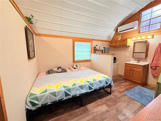 Bedroom featuring a wall mounted AC, lofted ceiling, light wood-style floors, and multiple windows | Image 15