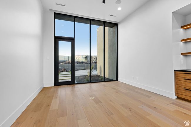 Empty room with light wood-type flooring, baseboards, a wall of windows, and visible vents | Image 21