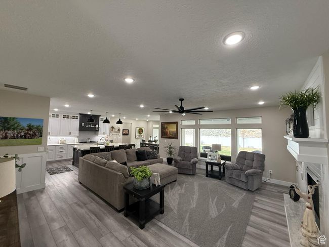 Living room with a premium fireplace, a textured ceiling, visible vents, a ceiling fan, and wood finished floors | Image 9