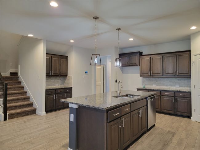 Kitchen with a sink, light wood-style floors, dark brown cabinetry, backsplash, and light stone countertops | Image 9