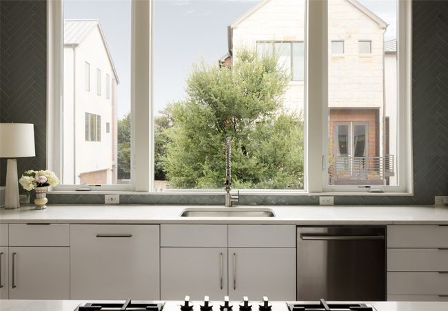 Kitchen with stainless steel dishwasher, light countertops, white cabinetry, and decorative backsplash | Image 17