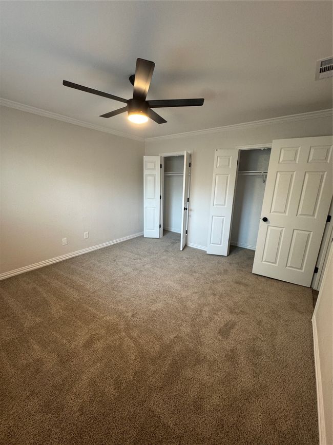 Unfurnished bedroom featuring two closets, carpet, baseboards, crown molding, and a ceiling fan | Image 10