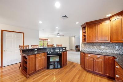 Kitchen with black oven, hanging light fixtures, light hardwood / wood-style floors, and dark stone countertops | Image 3