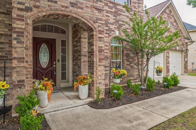 Doorway to property featuring brick siding, an attached garage, a shingled roof, and concrete driveway | Image 4