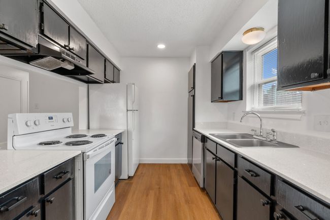 Kitchen with white range with electric cooktop, light countertops, light wood-type flooring, a textured ceiling, and extractor fan | Image 16