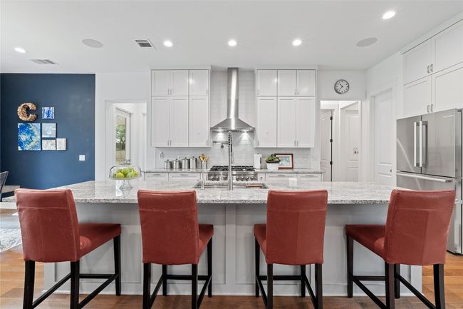 Kitchen with wall chimney exhaust hood, freestanding refrigerator, decorative backsplash, a large island with sink, and white cabinets | Image 5