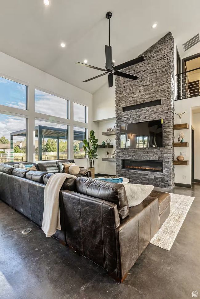 Living room featuring visible vents, a towering ceiling, ceiling fan, a stone fireplace, and concrete floors | Image 14
