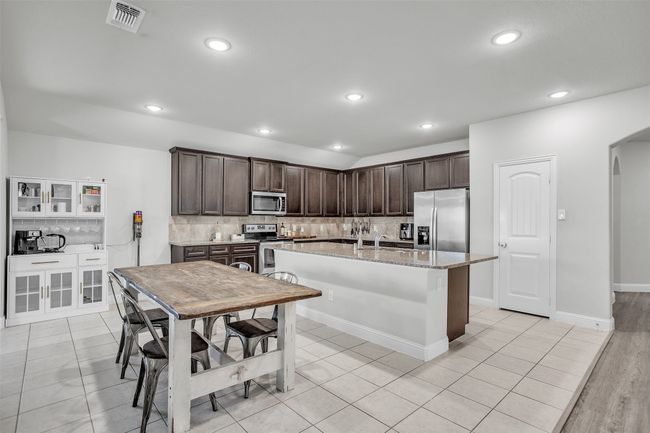 Kitchen featuring appliances with stainless steel finishes, arched walkways, dark brown cabinetry, backsplash, and recessed lighting | Image 6