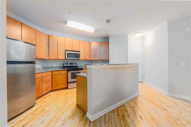 Kitchen featuring appliances with stainless steel finishes, light wood finished floors, ornamental molding, light stone countertops, and a kitchen island | Image 10