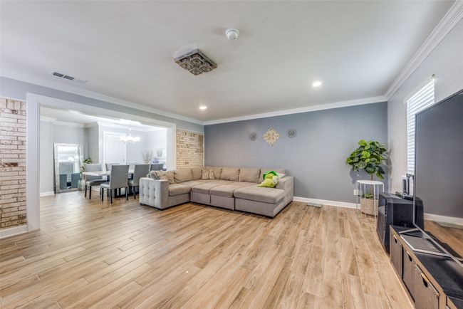 Living area with a chandelier, light wood-style floors, ornamental molding, recessed lighting, and brick wall | Image 8