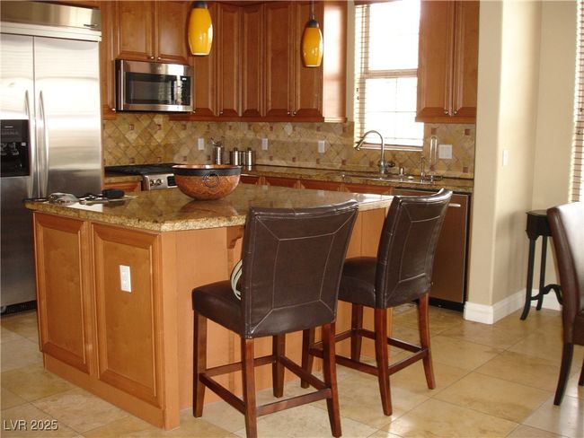 Kitchen featuring stainless steel appliances, brown cabinetry, stone counters, and a center island | Image 8