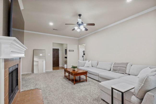 Living area featuring light colored carpet, visible vents, a tiled fireplace, ornamental molding, and baseboards | Image 9