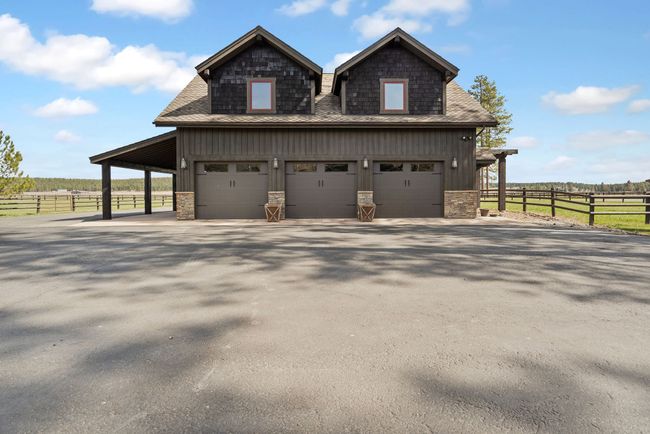 View of property exterior featuring stone siding, board and batten siding, an attached garage, aphalt driveway, and fence | Image 66
