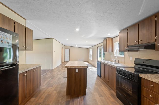 Kitchen featuring black appliances, under cabinet range hood, wood finished floors, a center island, and light countertops | Image 10