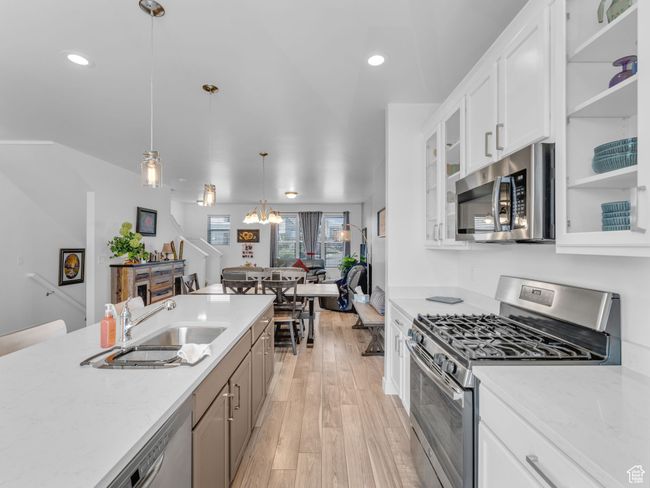 Kitchen featuring appliances with stainless steel finishes, light wood finished floors, glass insert cabinets, hanging light fixtures, and white cabinetry | Image 10