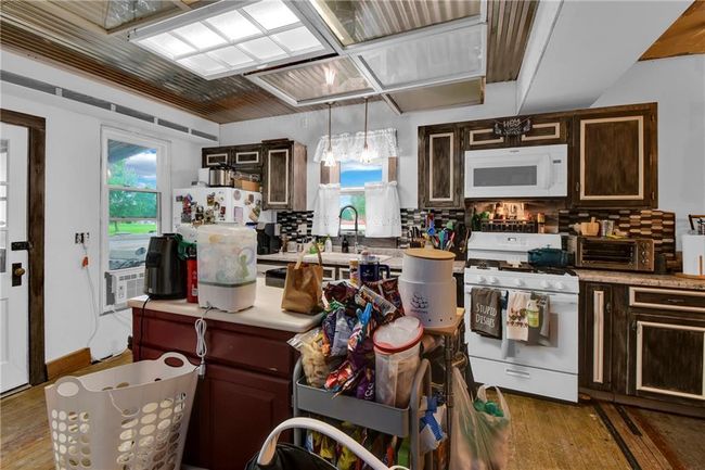 Kitchen featuring white appliances, wood-type flooring, tasteful backsplash, light countertops, and dark brown cabinetry | Image 7