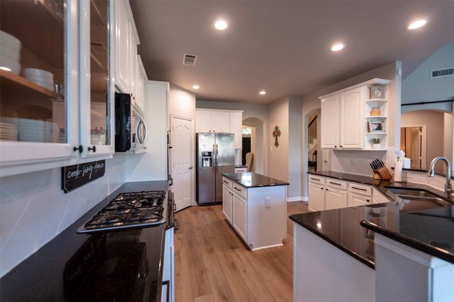 Kitchen featuring appliances with stainless steel finishes, arched walkways, dark countertops, open shelves, and light wood finished floors | Image 17