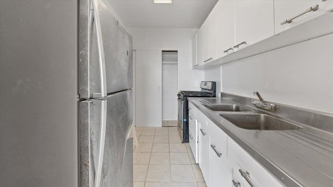 Kitchen with light tile patterned floors, white cabinetry, a sink, and appliances with stainless steel finishes | Image 6