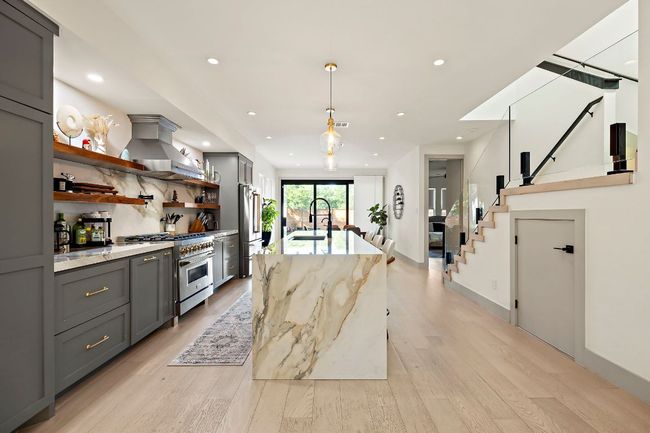 Kitchen with island exhaust hood, a sink, premium appliances, gray cabinets, and open shelves | Image 6