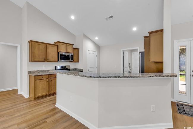 Kitchen featuring appliances with stainless steel finishes, light wood-type flooring, light stone counters, brown cabinets, and recessed lighting | Image 8
