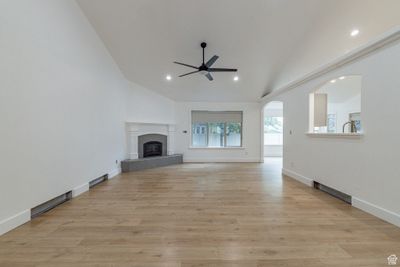 Unfurnished living room featuring a tile fireplace, high vaulted ceiling, ceiling fan, and light hardwood / wood-style flooring | Image 2