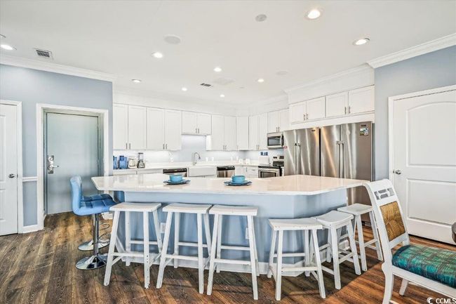 Kitchen featuring white cabinetry, ornamental molding, a breakfast bar, recessed lighting, and a large island | Image 7