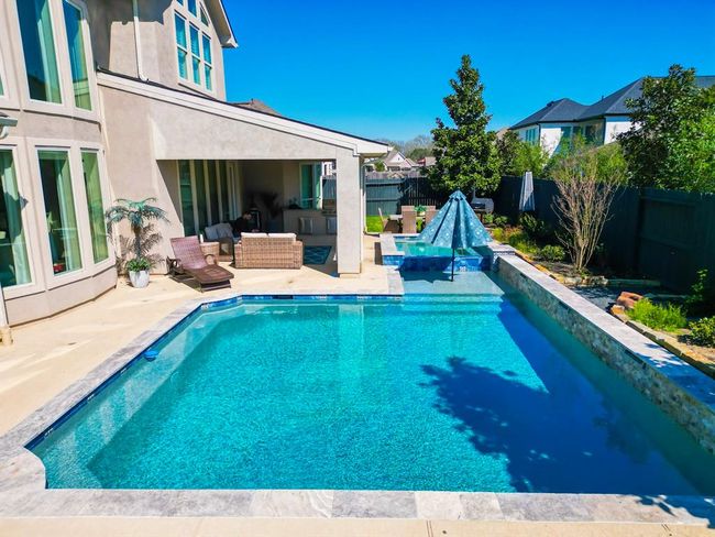 This photo showcases a modern backyard with a sparkling in-ground swimming pool and a cozy covered patio area, perfect for relaxation and entertaining. The space is complemented by surrounding greenery and offers a private, inviting atmosphere. | Image 45
