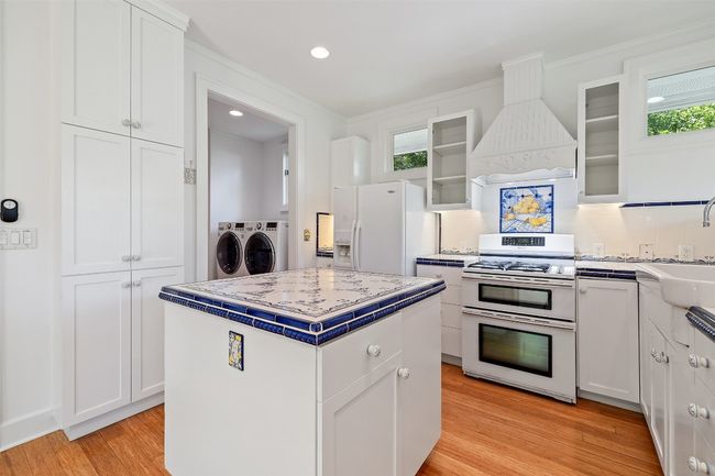Kitchen featuring premium range hood, washer and clothes dryer, white cabinetry, and white appliances | Image 8