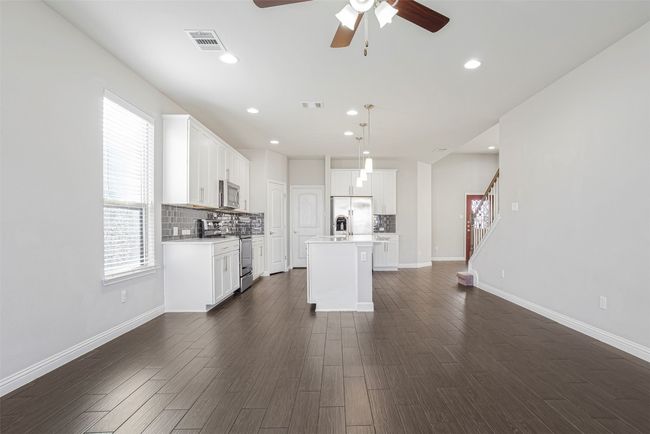 Kitchen with dark wood-type flooring, ceiling fan, stainless steel appliances, a kitchen island with sink, and light countertops | Image 15