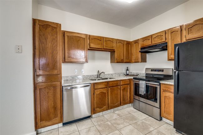 Kitchen with brown cabinets, appliances with stainless steel finishes, under cabinet range hood, a sink, and light tile patterned floors | Image 10