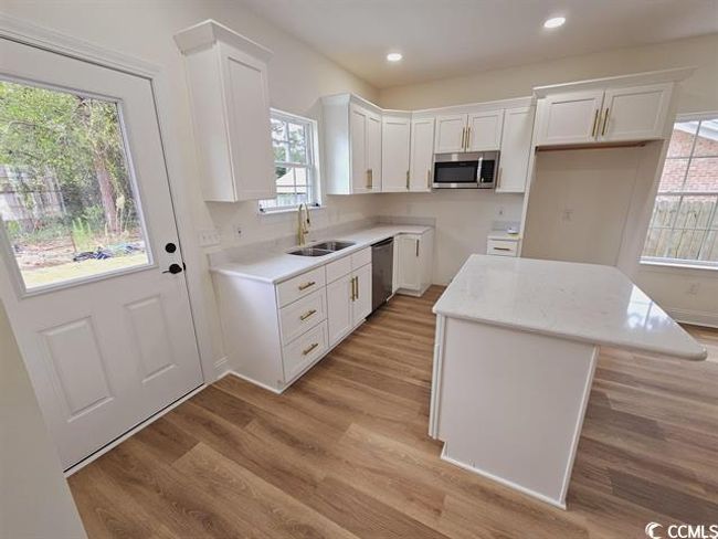 Kitchen with white cabinets, a center island, stainless steel appliances, light countertops, and a sink | Image 26