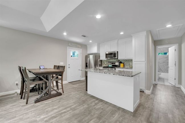 Kitchen with light wood-type flooring, white cabinets, appliances with stainless steel finishes, and a kitchen island with sink | Image 16