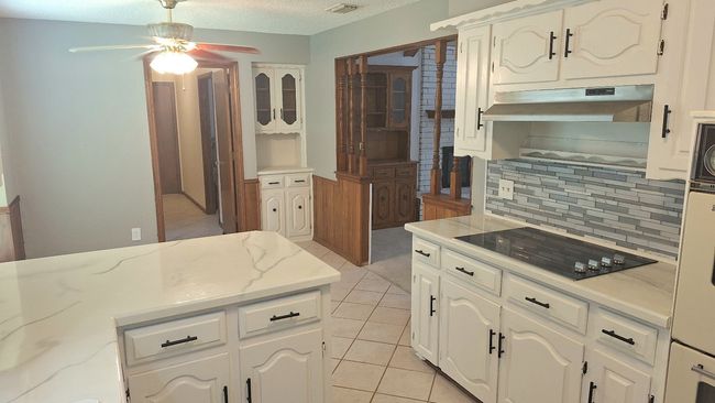 Kitchen featuring black electric cooktop, under cabinet range hood, ceiling fan, decorative backsplash, and light tile patterned floors | Image 7