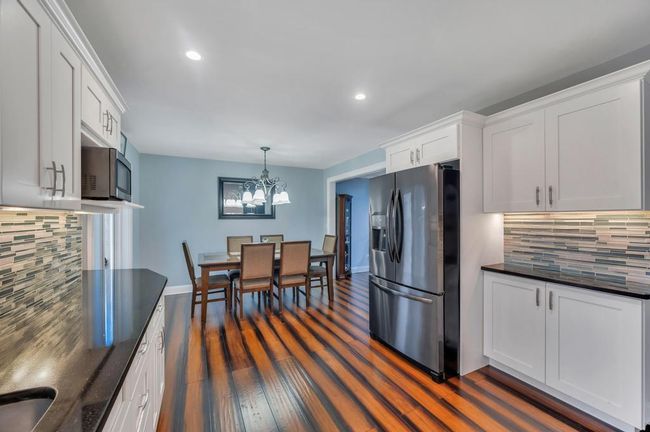 Kitchen featuring stainless steel microwave, dark wood-style flooring, refrigerator with ice dispenser, dark countertops, and a notable chandelier | Image 4